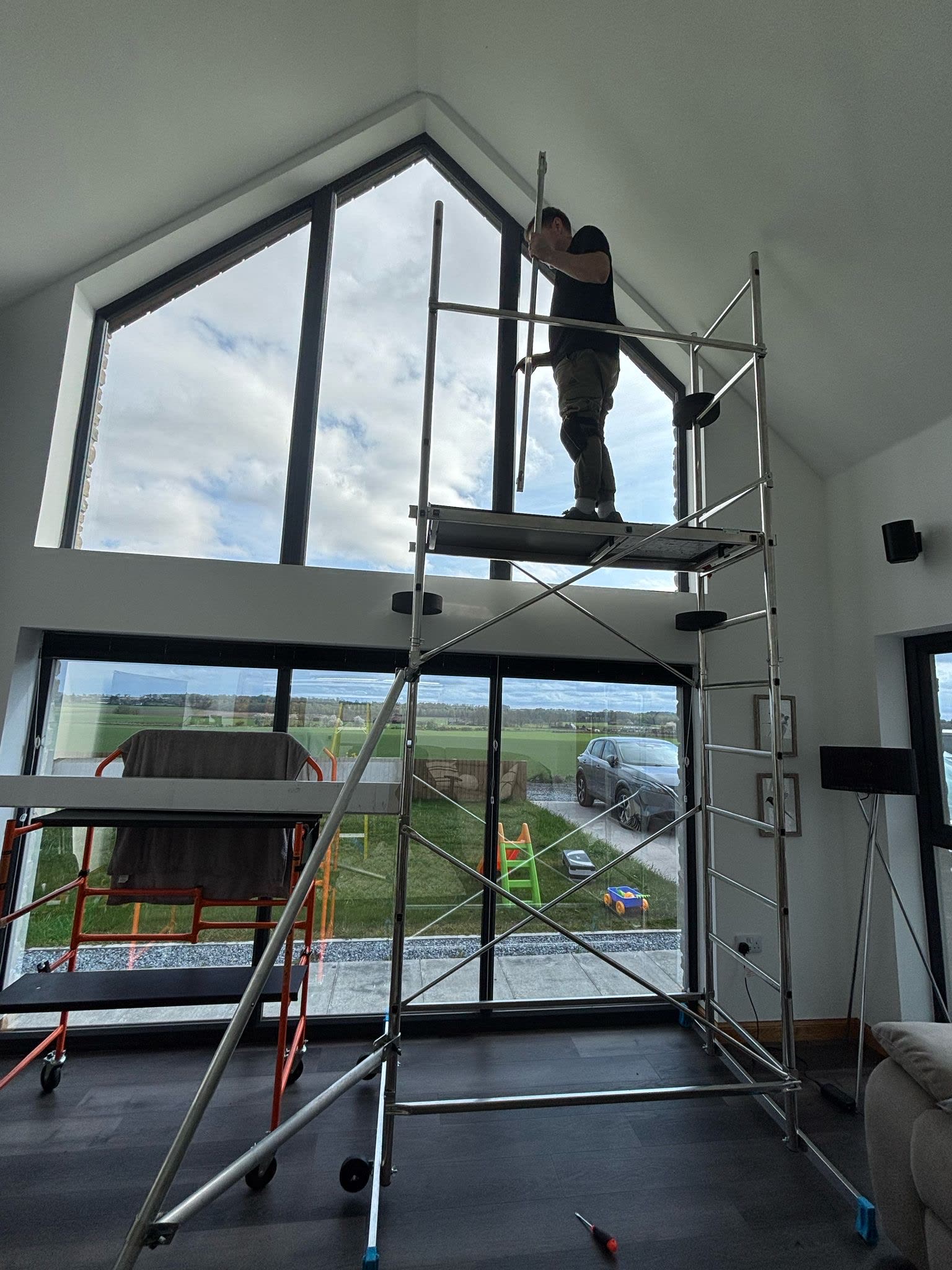 Window Tint Company installer fitting film on a tall gable window from interior scaffolding